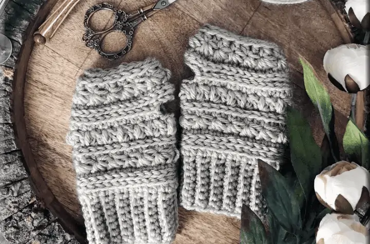 Grey crochet fingerless gloves on a wooden backdrop.