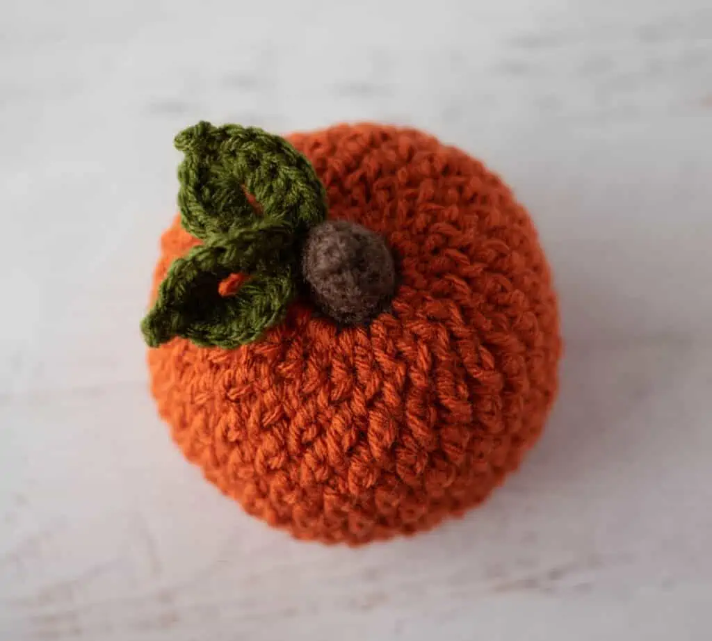 Top down view of Orange crochet textured pumpkin with brown stem and green leaves