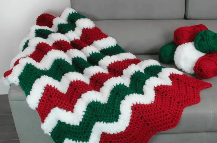 A red, green, and white squiggle blanket laying on a grey couch.
