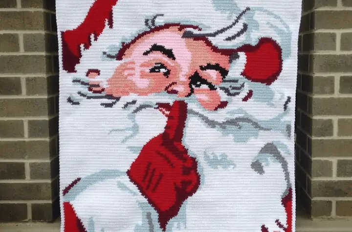 Santa crochet throw blanket doing the hush motion.