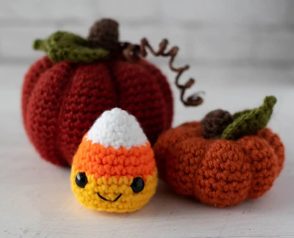 Crochet candy corn with two crochet pumpkins in fall colors of orange, white, yellow.