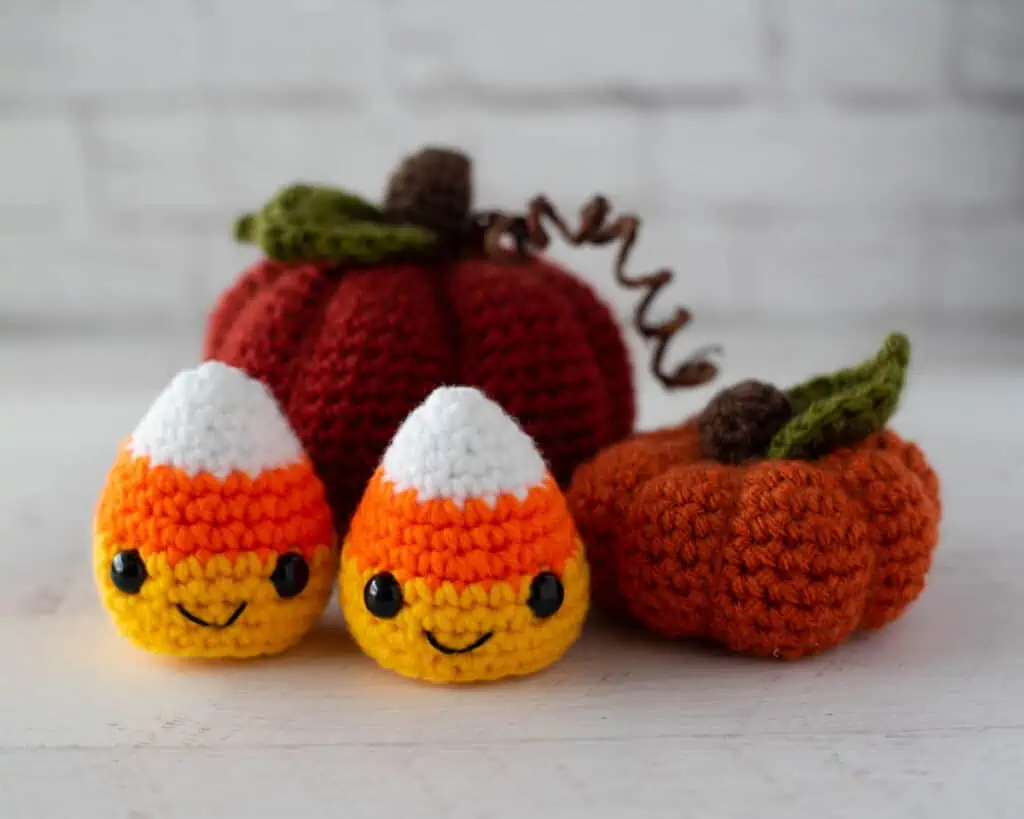 Crochet candy corn with two crochet pumpkins in fall colors of orange, white, yellow.