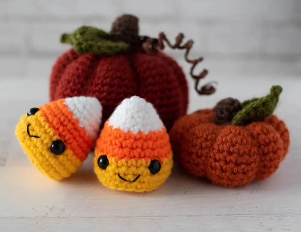 Crochet candy corn with two crochet pumpkins in fall colors of orange, white, yellow.