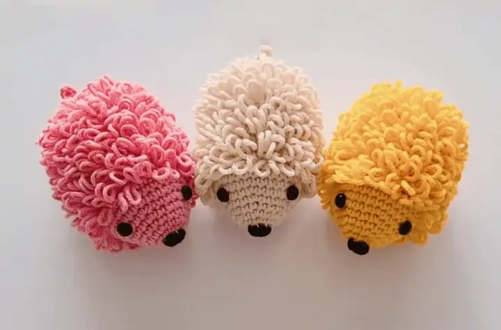 Three crochet hedgehods, one pink, one white, and one yellow.