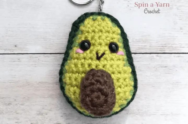 Crochet avocado keychin with black eyes, blush marks, ad a little smile.