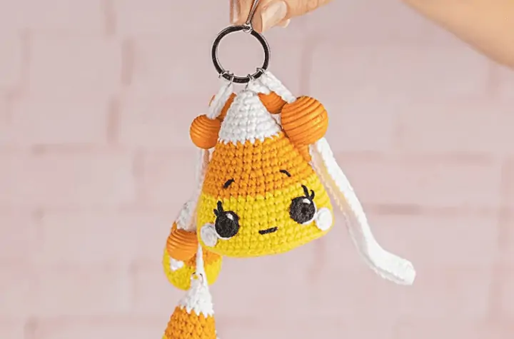 Crochet candy corn keychain that features alarge candy corn with a face on it, two smalled candy corns dangling off the side, and orange beads.
