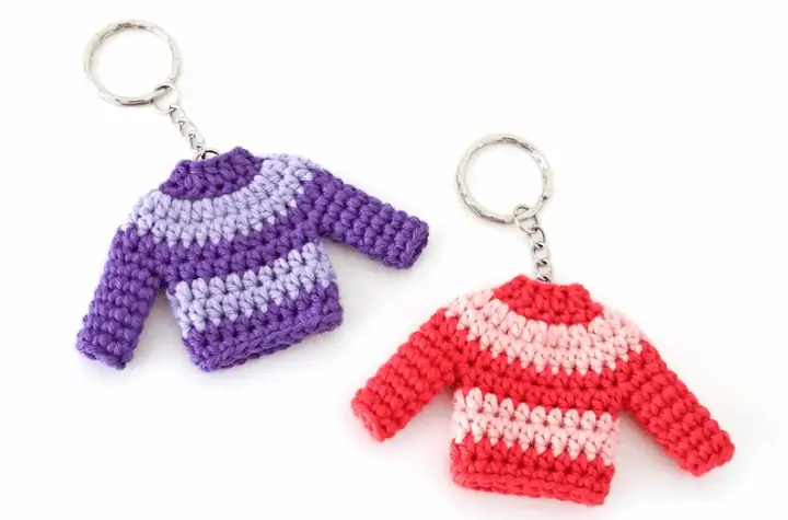 Two crochet sweater body keychains, one different shades of purple and one different shades of pink.