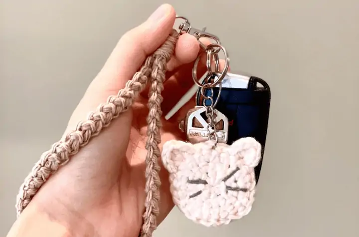 Hand holding a wristlet with a flat crochet cat face keychain and car keys.