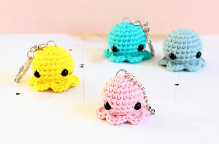Four little crochet octopus keychains in yellow. bright blue, medium blue, and pink.