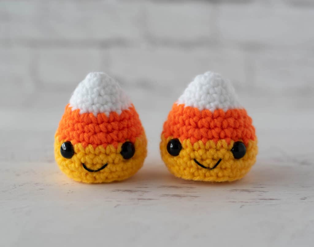 Two crochet candy corn with black eyes and smile in white, orange and yellow