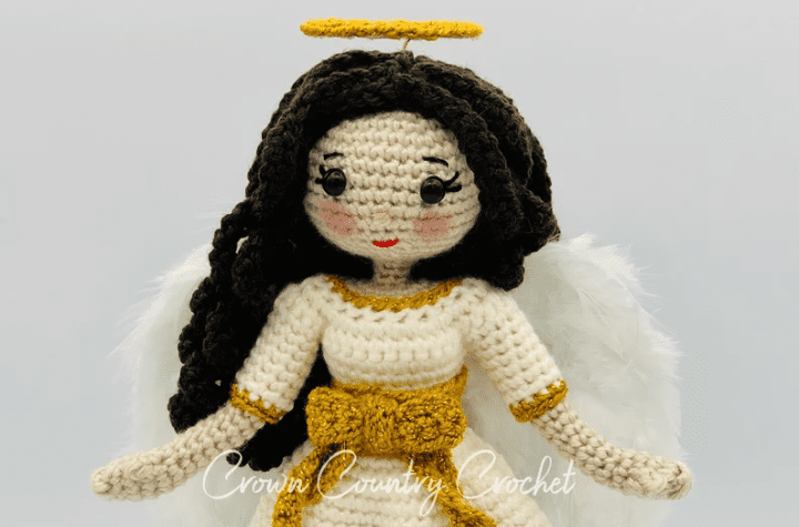 A crochet angel with curly brown hair and feather wings.