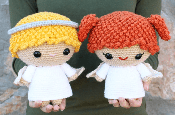 Two large crochet angel amigurumis, one with blonde hair and one that is a red head.