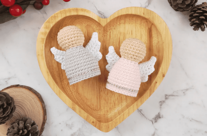 Two crochet angels in a heart-shapped wooden bowl.