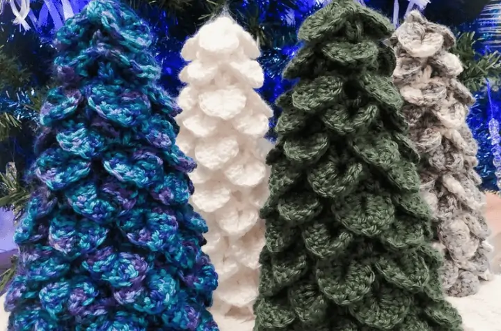 Four different crochet christmas trees looking to be made up of individual leaf patterns, there is one green tree, one a blue purple, one white, and one grey.
