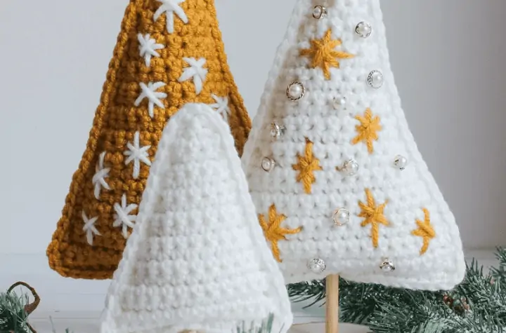 Triangel-shaped crochet Christmas trees on a stick. one plain white, one white with gold star ornaments, and one gold with white star ornaments.