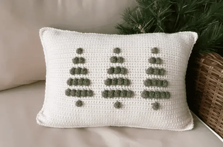 A small rectangular pillow with three crochet trees on it with an all white background.