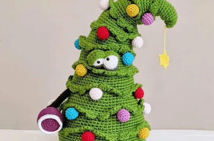 A crochet Christmas tree that looks like tit enjoyed the holiday party a little too much. it also has a wine cup upside down in it's hand.