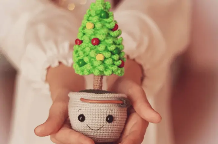 Small christmas tree amigurumi with a little face on the planter.