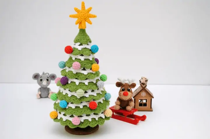 Crochet Christmas tree with circular Christmas ornaments and a star on top ad well as a small reindeer and a small mouse amigurumi.