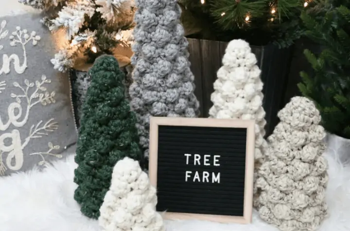 Five crochet Christmas trees, one that is traditional green, and the rest are in varying degrees of white and off white.