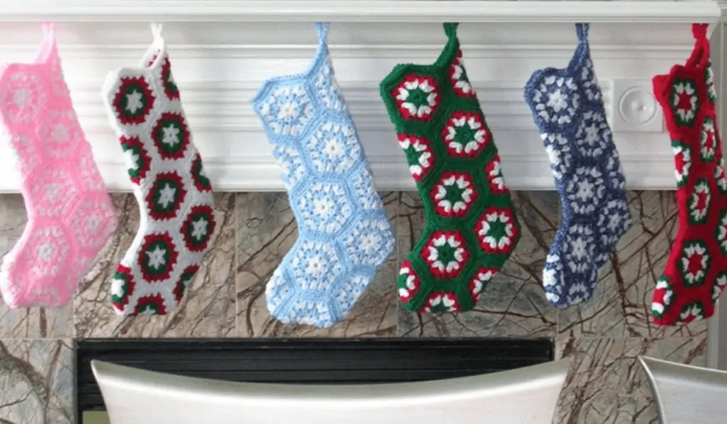 Six stockings handing on a mantle, one that is pink and one, one that is white, red, and green, one that is blue and white, one that is green, red, and white, one that is darker blue and white, one that is red, green, and white.