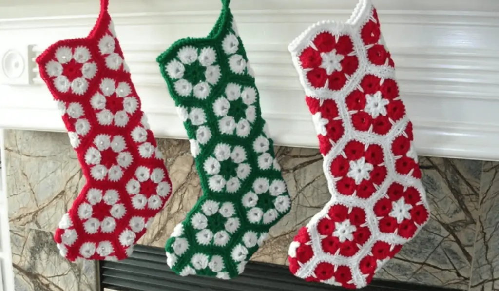 Three flower granny square stockings, one that is a red stocking with white flowers, one that is a green stocking with white flowers, and one that is a white stocking with red flowers.