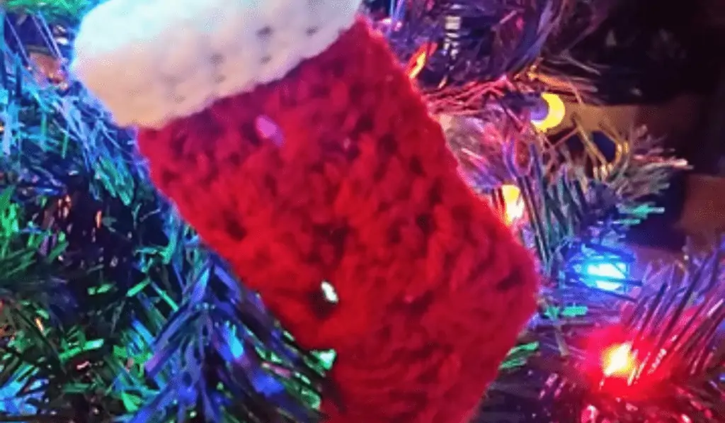 A mini all red granny square stocking this is hung on a Christmas tree.