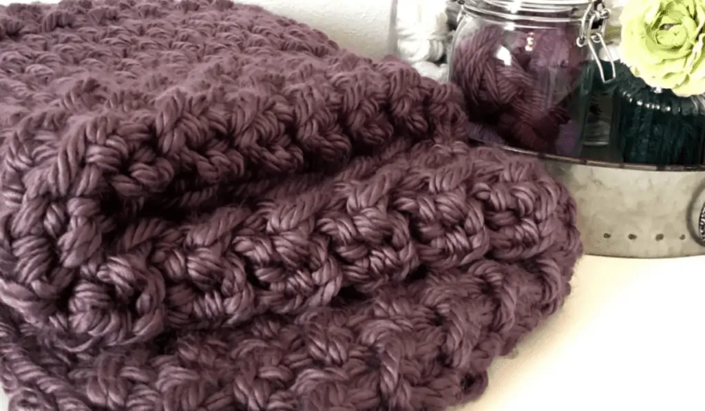 A purple blanket folded up and using chunky yarn.