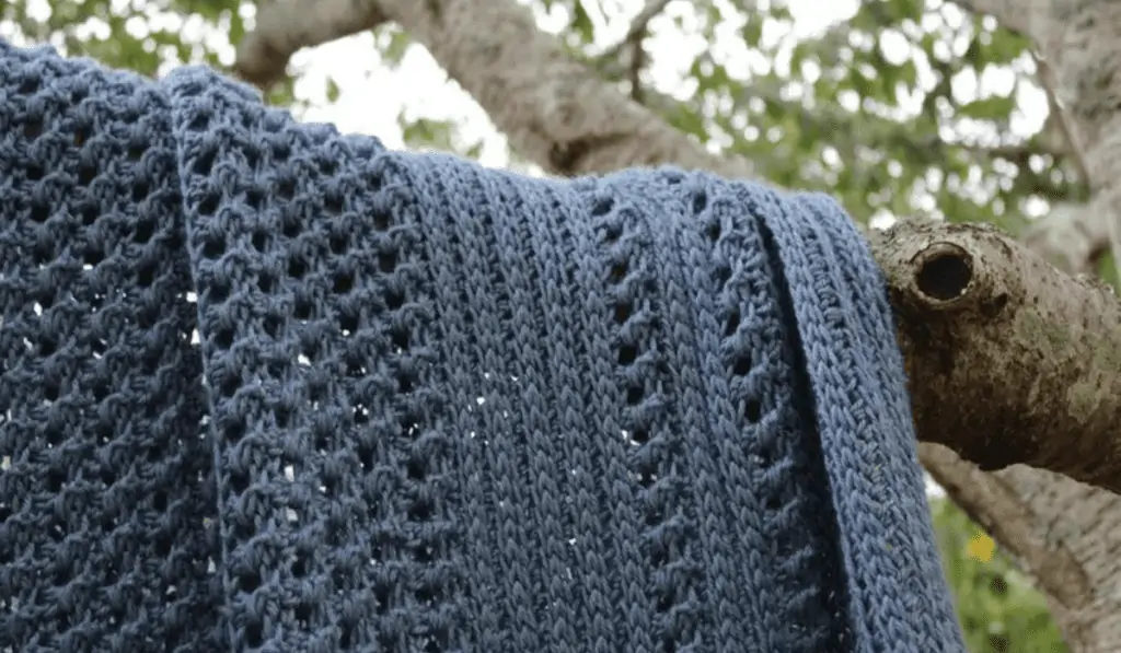 a navy blue crochet blanket drapped over the branch of a tree.