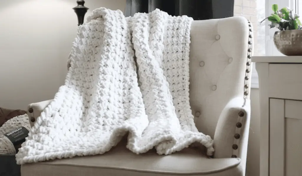 A white crochet blanket drapped over the back of a chair.