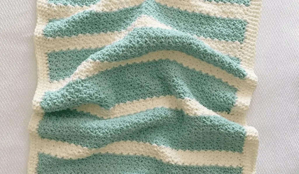 A baby blanket with off white stripes and blocks of blue yarn.