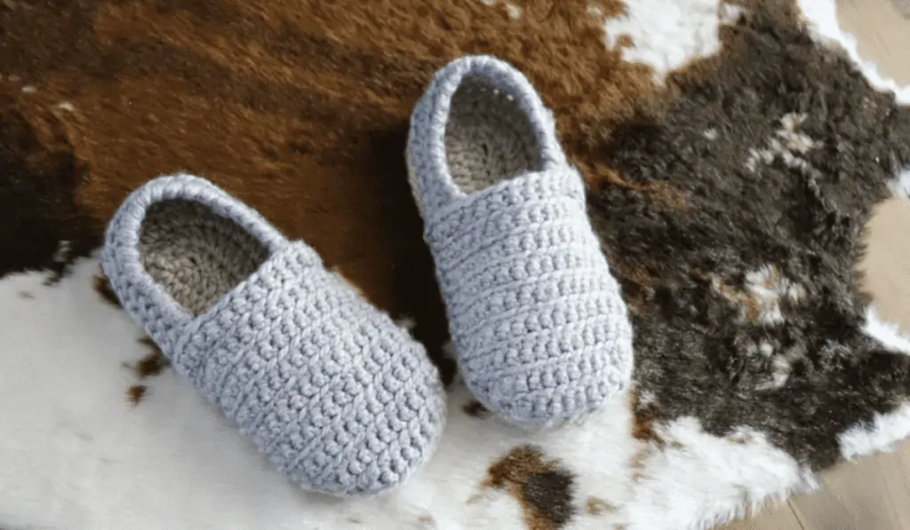 Little grey slippers laying on a cow rug.