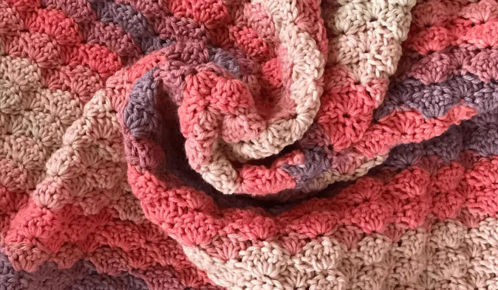 A blanket made out of shade of pink and purple yarn.