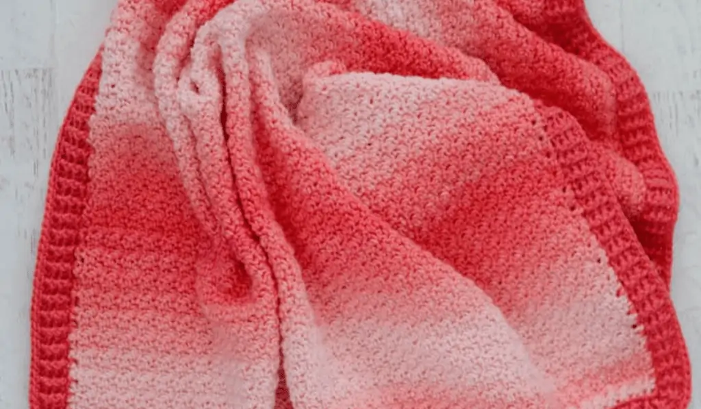 A crochet blanket with different shades of pink in a gradient.