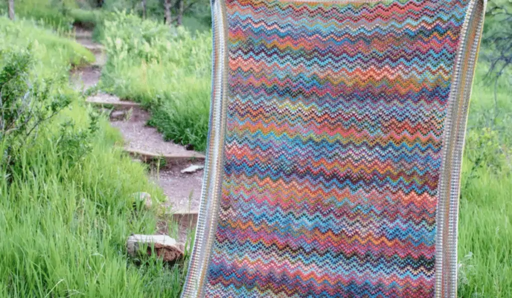 A colorful crochet blanket being held up off a hiking trail.