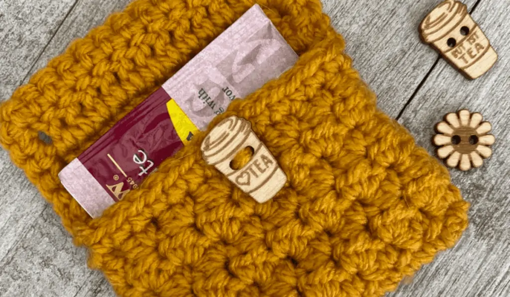 Yellow crochet gift card holder white a wooden button that looks like a warm tea cup.