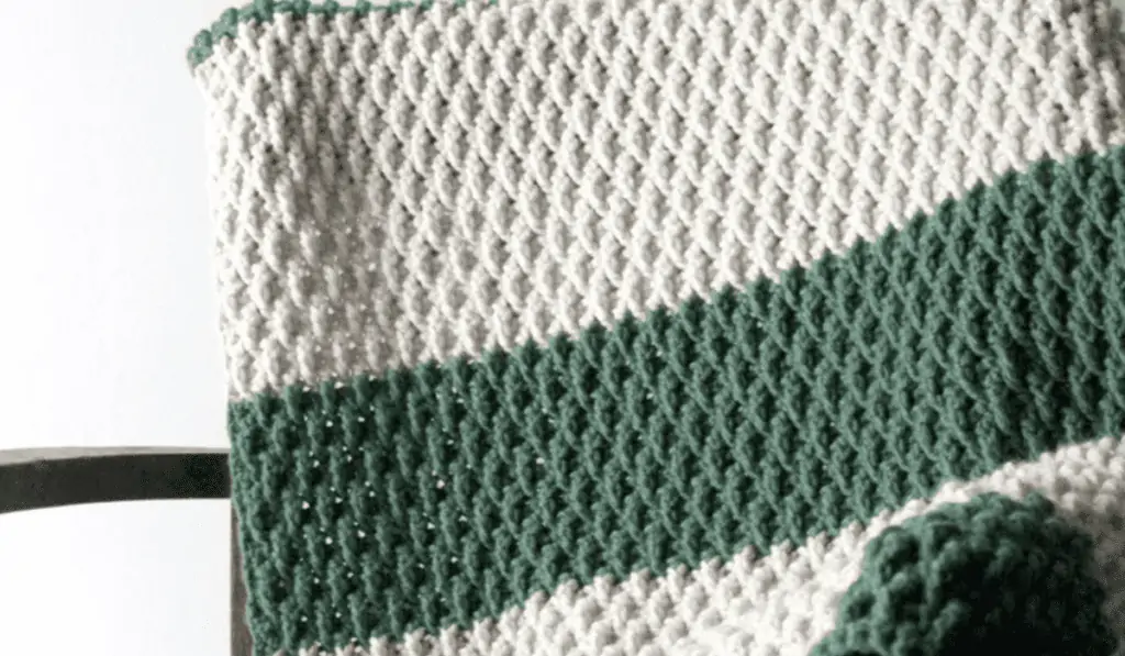 A crochet blanket with large stripes of white and green