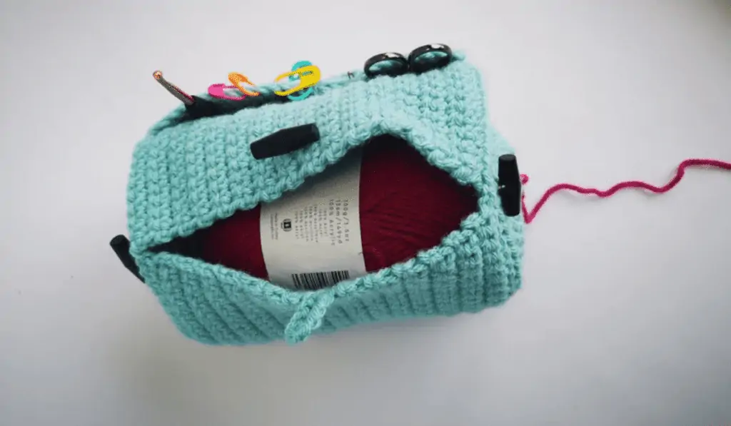 Crochet yarn bag with blue yarn and a pocket for your crochet hook, stitch markets, and sizzers.