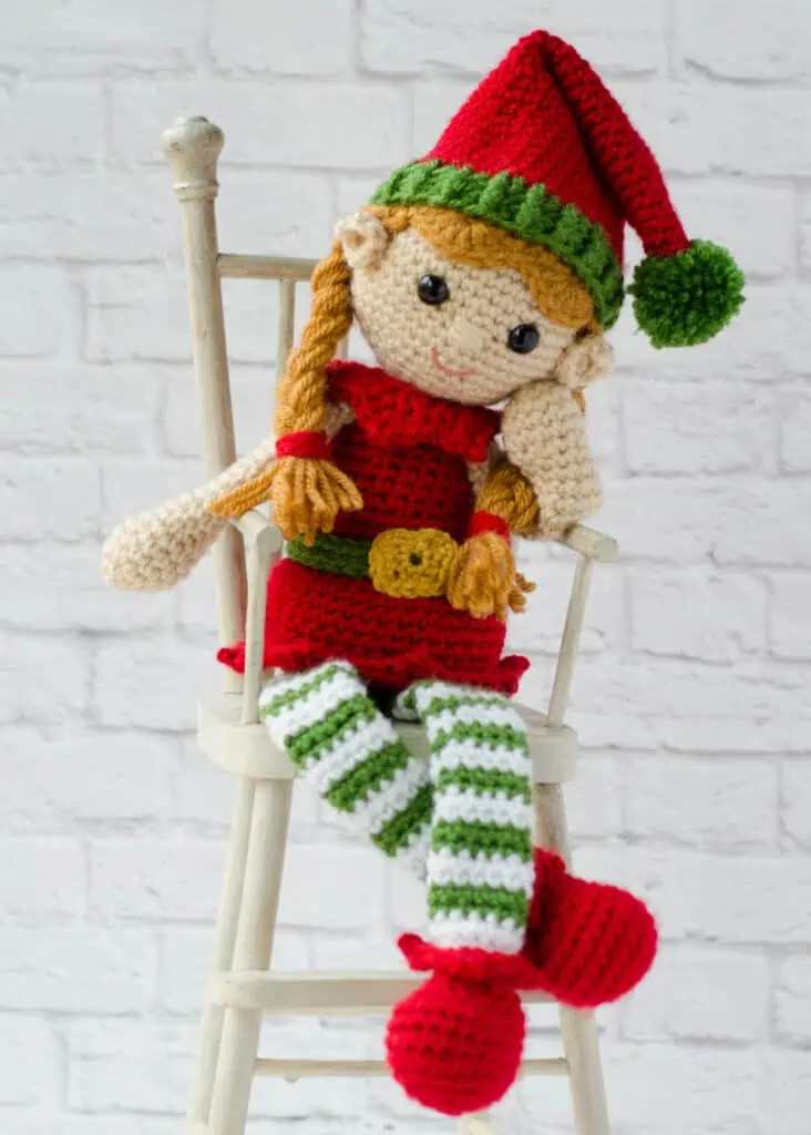 crochet elf in red, green and white sitting on a chair
