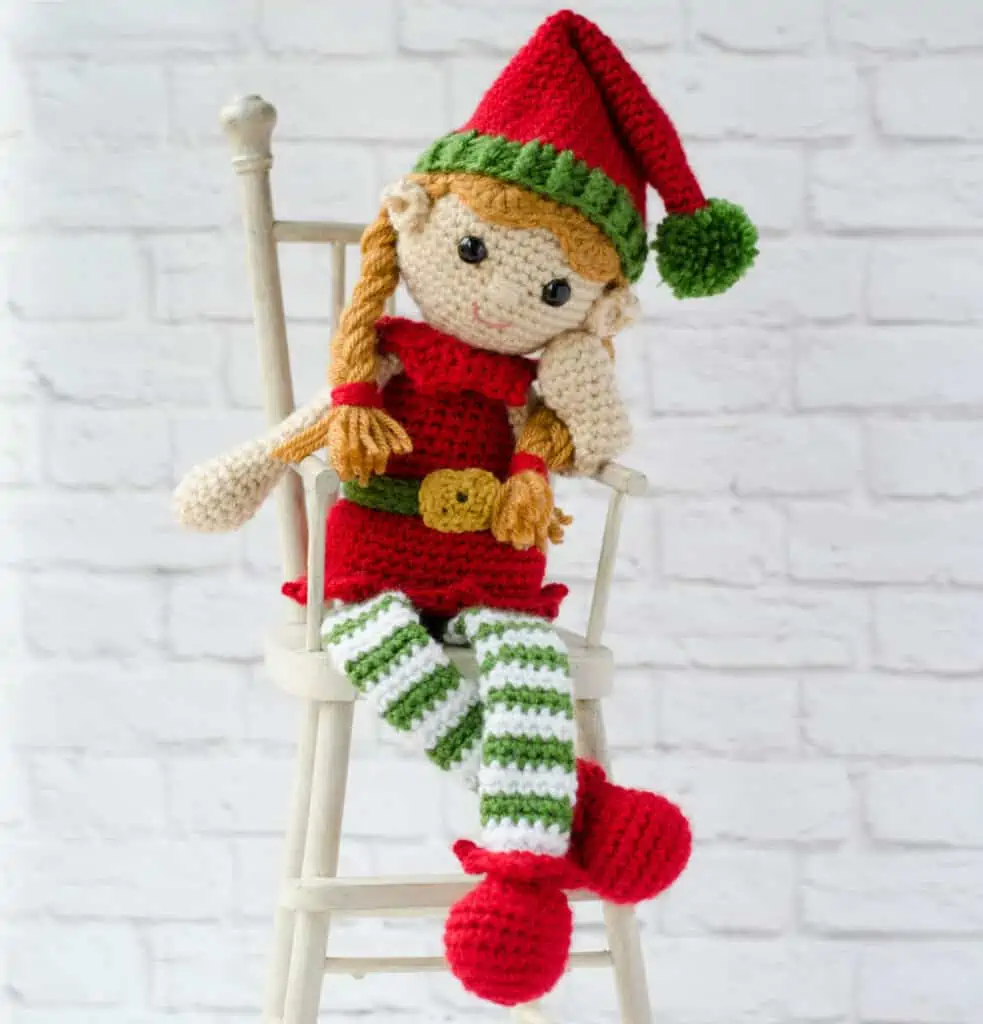 crochet elf in red, green and white sitting on a chair