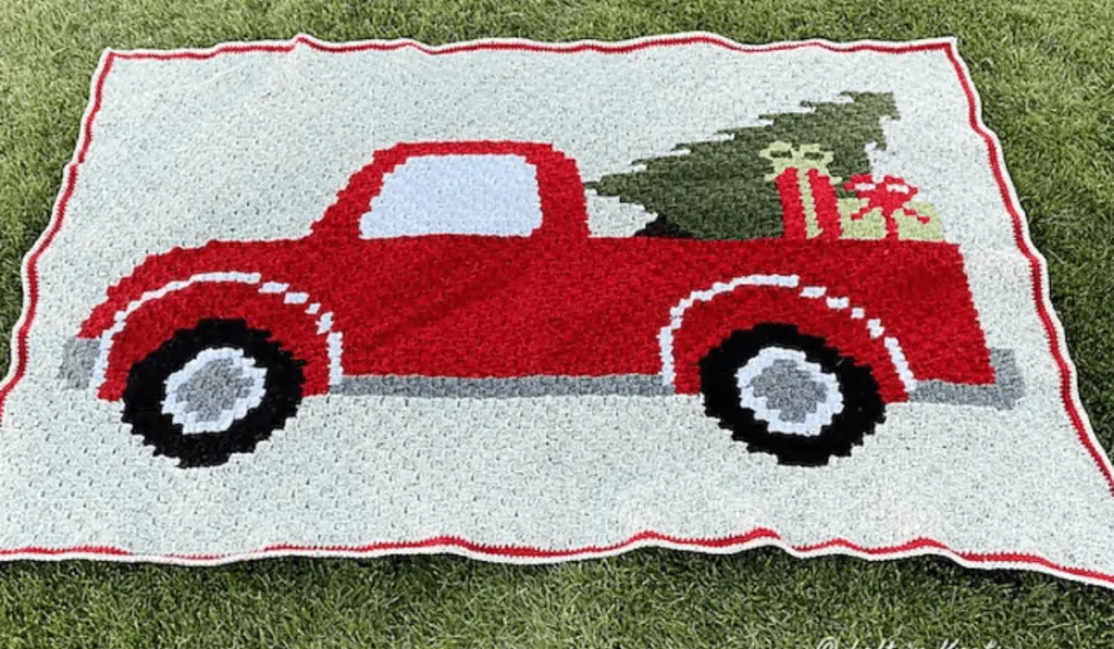 A blanket featuring a red pickup truck with a pine tree and presents in the back.