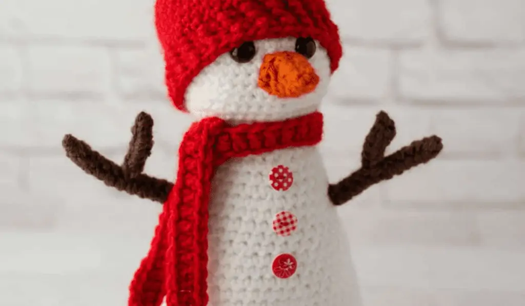 Crochet snowman amigurumi with a red hat and scarf and red buttons.