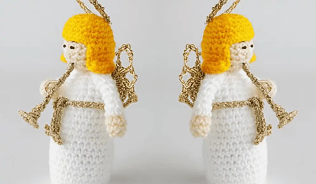 Two crochet angels facing away from each other and blowing a horn with a little gold halo and gold wings.