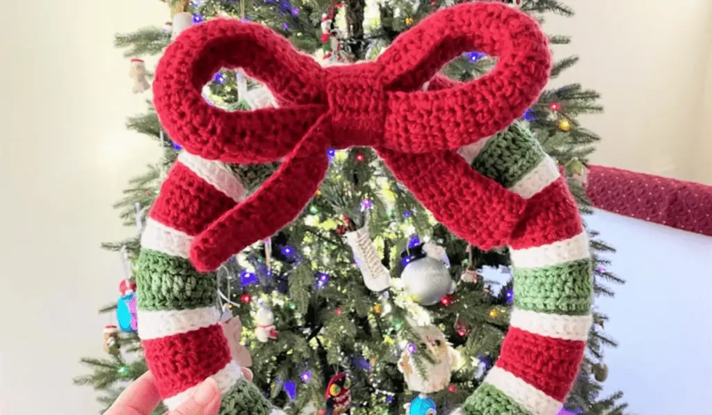 A crochet wreath with stripes of red, white, and green, and a large red bow on the top.