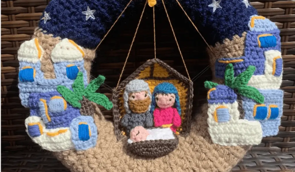 A crochet wreath with a nativity scene, featuring the holy family as well as two buildings.