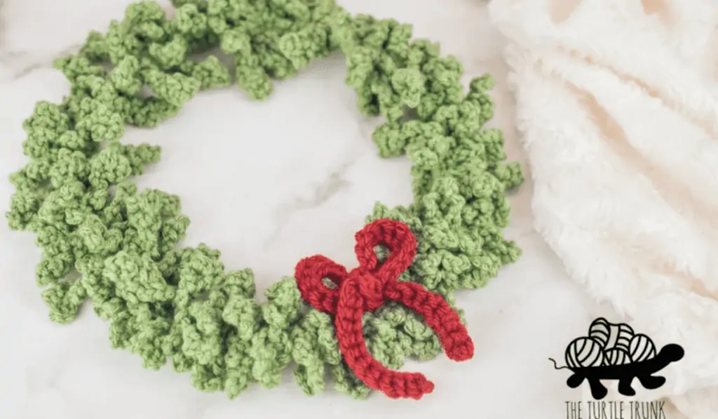 A classic crochet wreath with crocheted leaves and a red bow.
