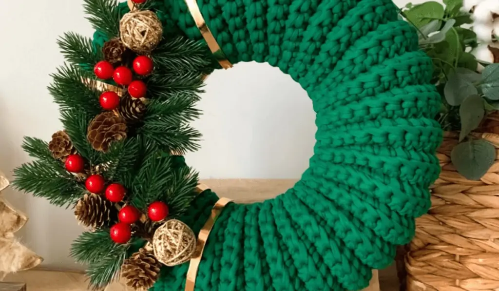 A green crochet wreath with plastic leaves and holy berries as well as real pine cones and little yarn balls.