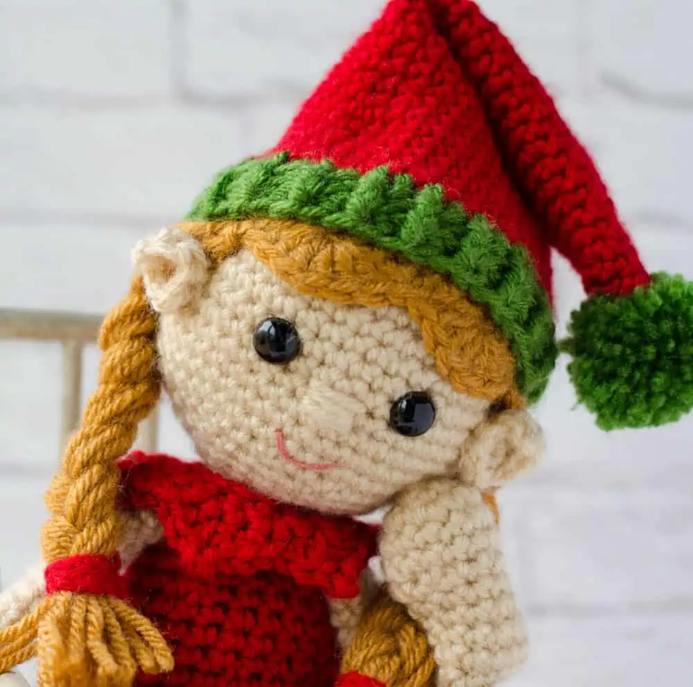 Close up of pigtailed crochet elf with a red hat and green trim and a red dress