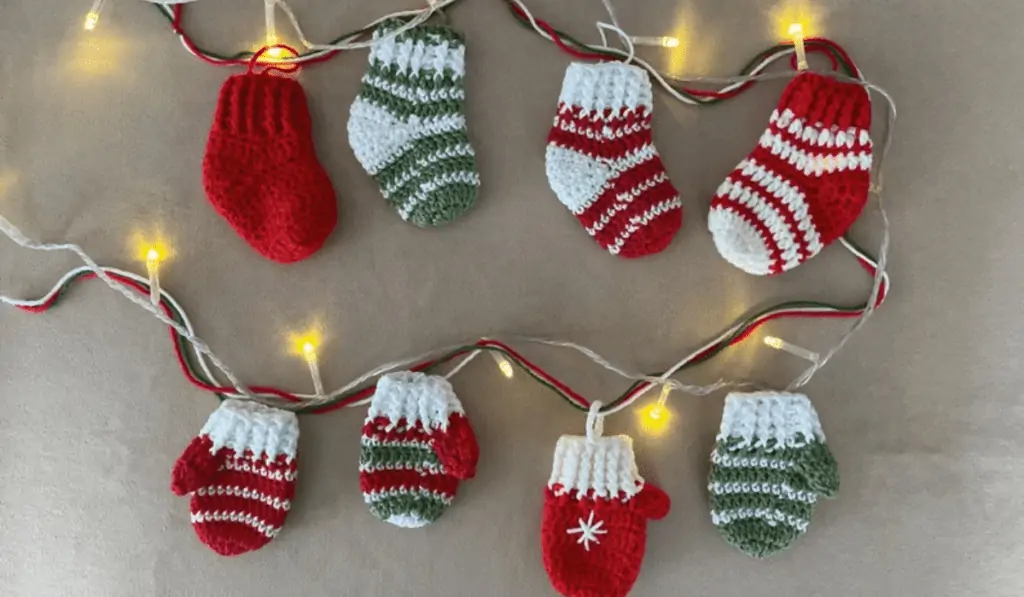 A garland that is mixed with fairy lights and had stocking and mittons hanging from it.