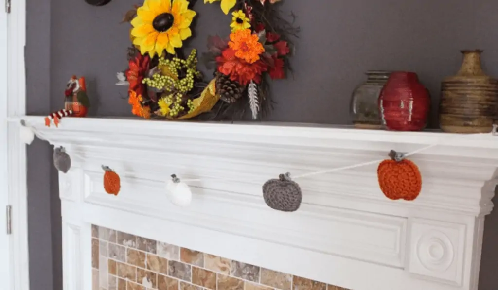 White, grey, and orange crochet pumpkins hanging on a fireplace mantle.